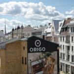 View of Riga buildings with ORIGO sign, showcasing city architecture.